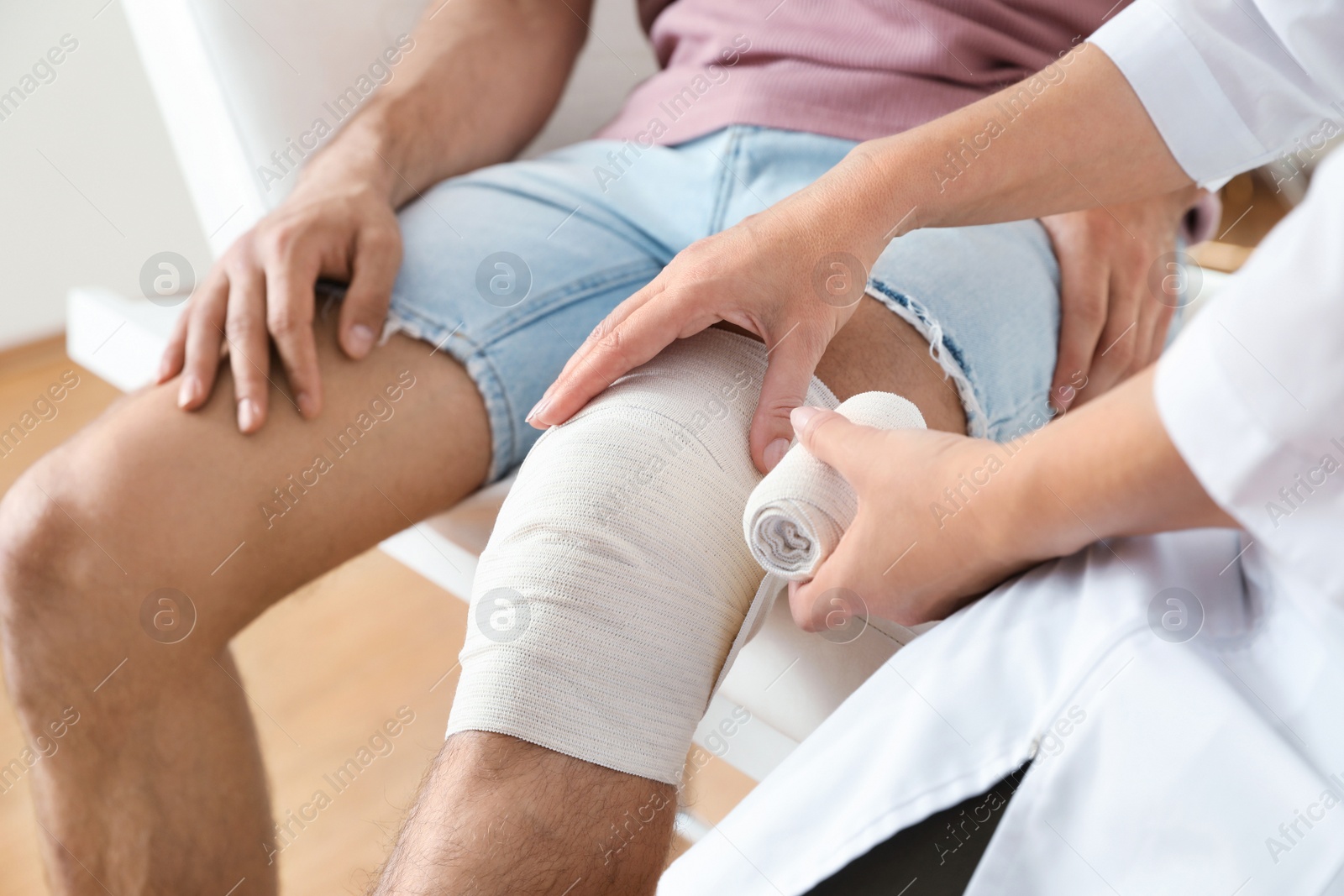 Photo of Doctor applying bandage to patient's knee in clinic, closeup