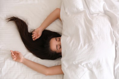 Photo of Young woman hiding under warm white blanket in bed, top view