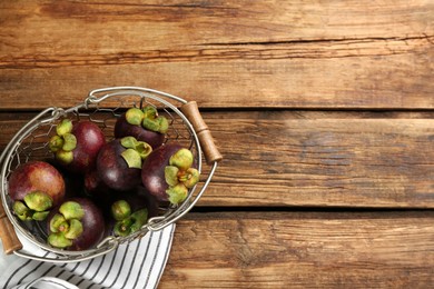 Photo of Fresh ripe mangosteen fruits in metal basket on wooden table, top view. Space for text