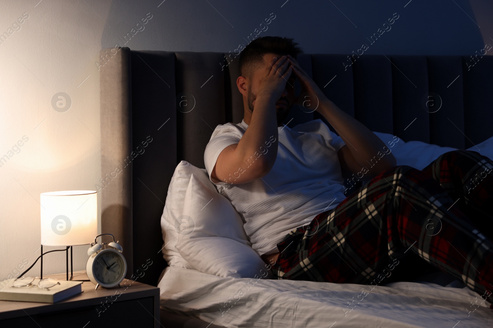 Photo of Man covering face with hands on bed. Insomnia problem
