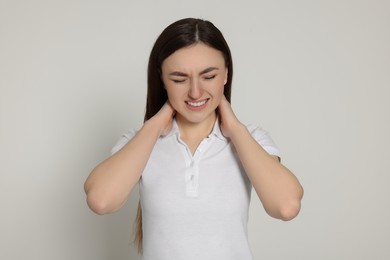Photo of Young woman suffering from neck pain on light grey background. Arthritis symptoms
