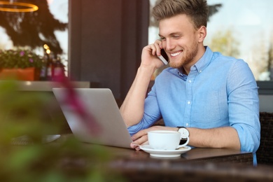 Photo of Handsome young man with laptop sitting at table in cafe outdoors