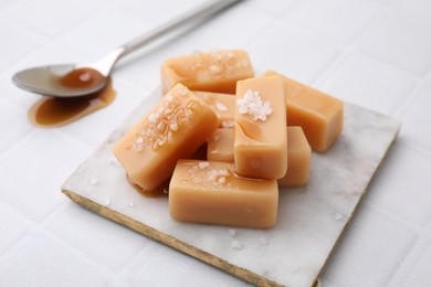 Photo of Delicious candies with sea salt and caramel sauce on white tiled table, closeup