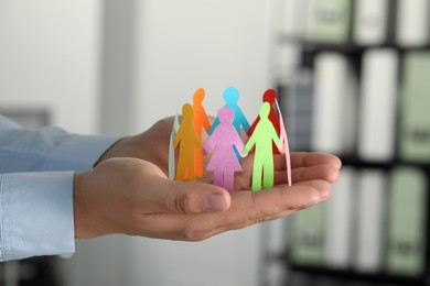 Photo of Man holding paper human figures in office, closeup. Diversity and Inclusion concept