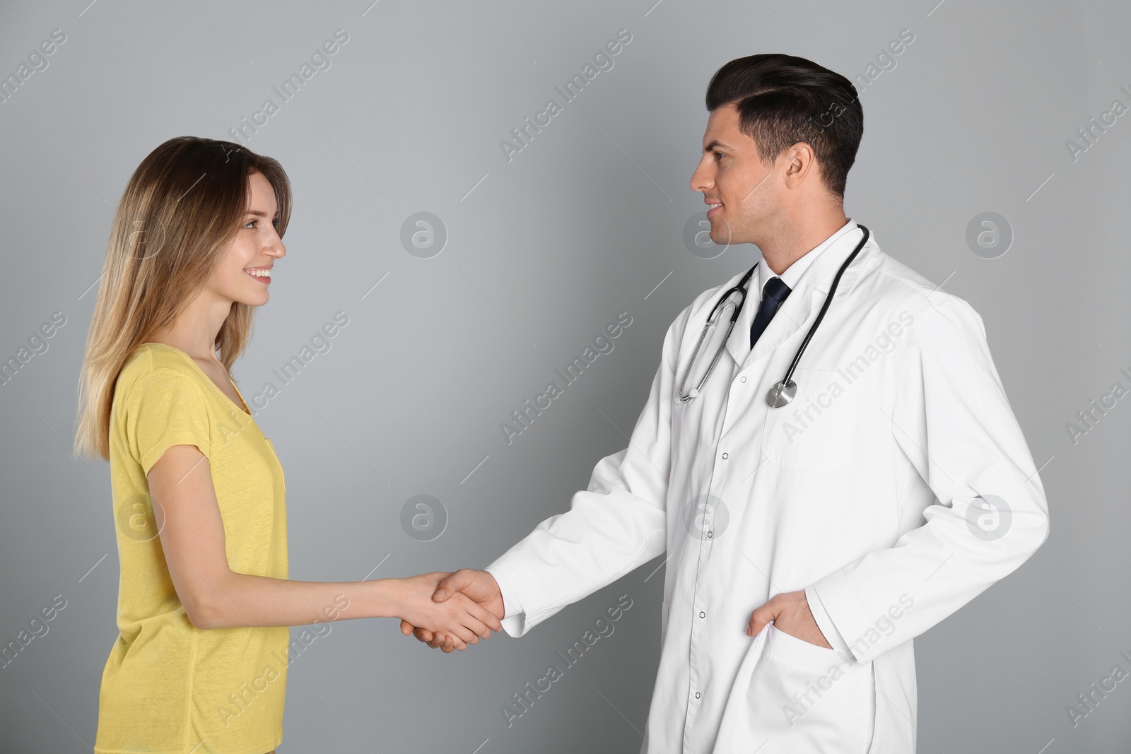 Photo of Doctor and patient shaking hands on light grey background