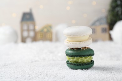 Different decorated Christmas macarons on table with artificial snow, space for text