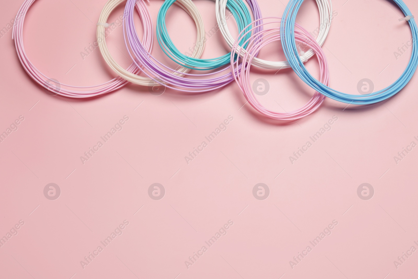 Photo of Colorful plastic filaments for 3D pen on pink background, flat lay. Space for text