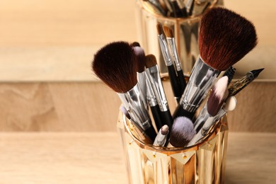 Photo of Set of professional makeup brushes near mirror on wooden table, closeup