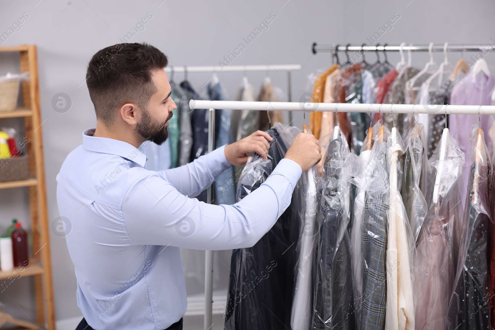 Photo of Dry-cleaning service. Worker choosing clothes from rack indoors