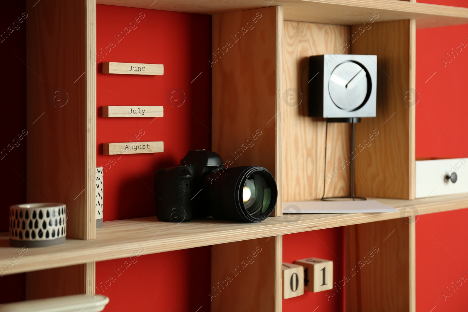 Photo of Stylish wooden shelf with camera and decorative elements on red wall