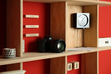 Stylish wooden shelf with camera and decorative elements on red wall