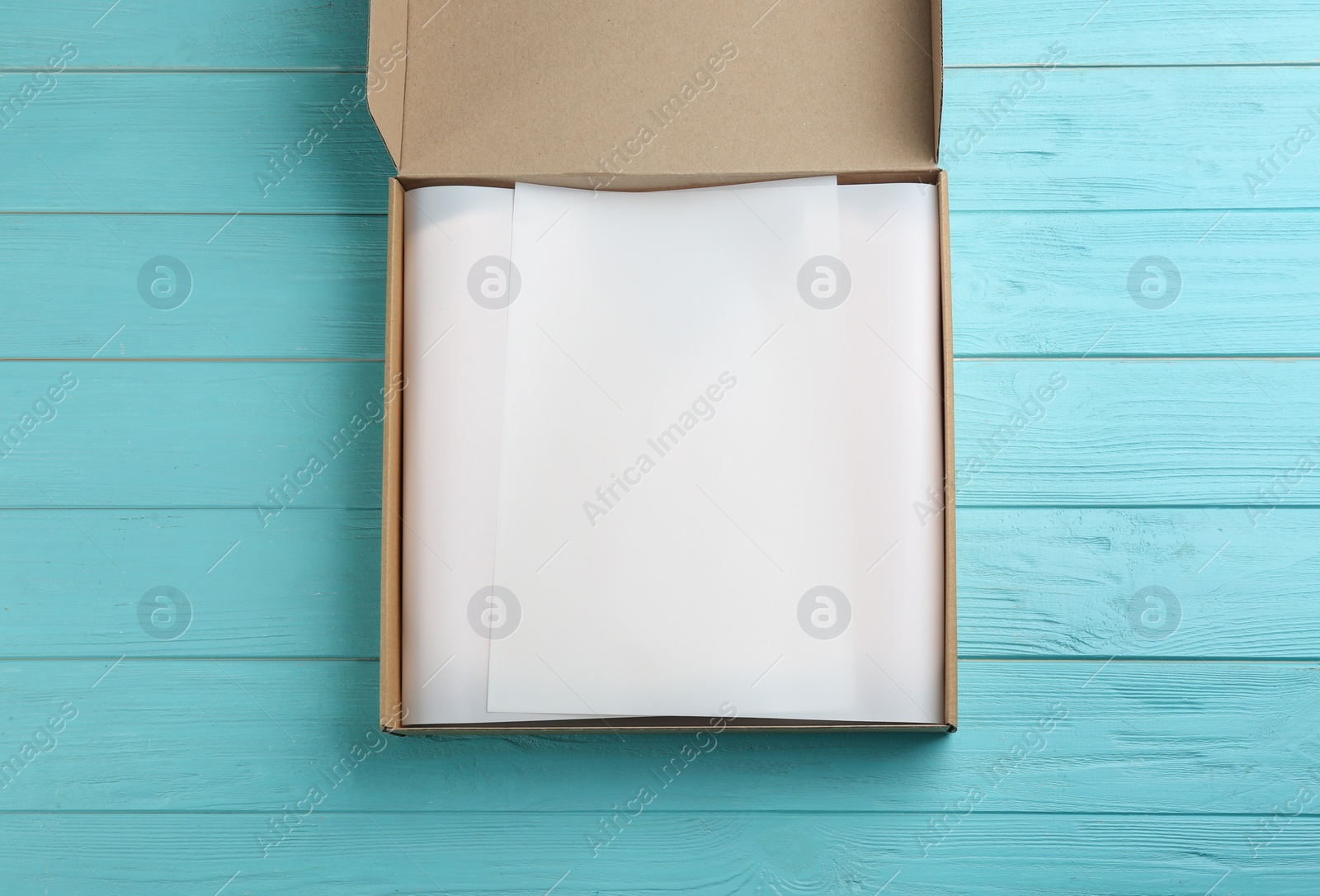 Photo of Cardboard box with parchment on light blue wooden background, top view