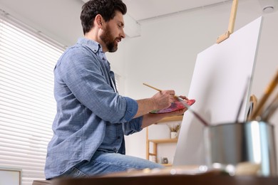 Photo of Man painting in studio, low angle view. Using easel to hold canvas