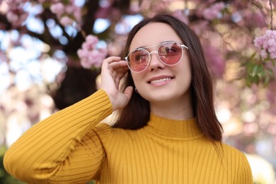 Beautiful woman in sunglasses near blossoming tree on spring day