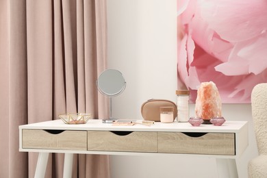 Photo of Dressing table with mirror, cosmetic products, jewelry and burning candles in makeup room