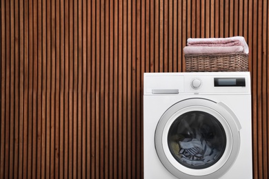 Photo of Washing machine and laundry basket with towels near wooden wall. Space for text