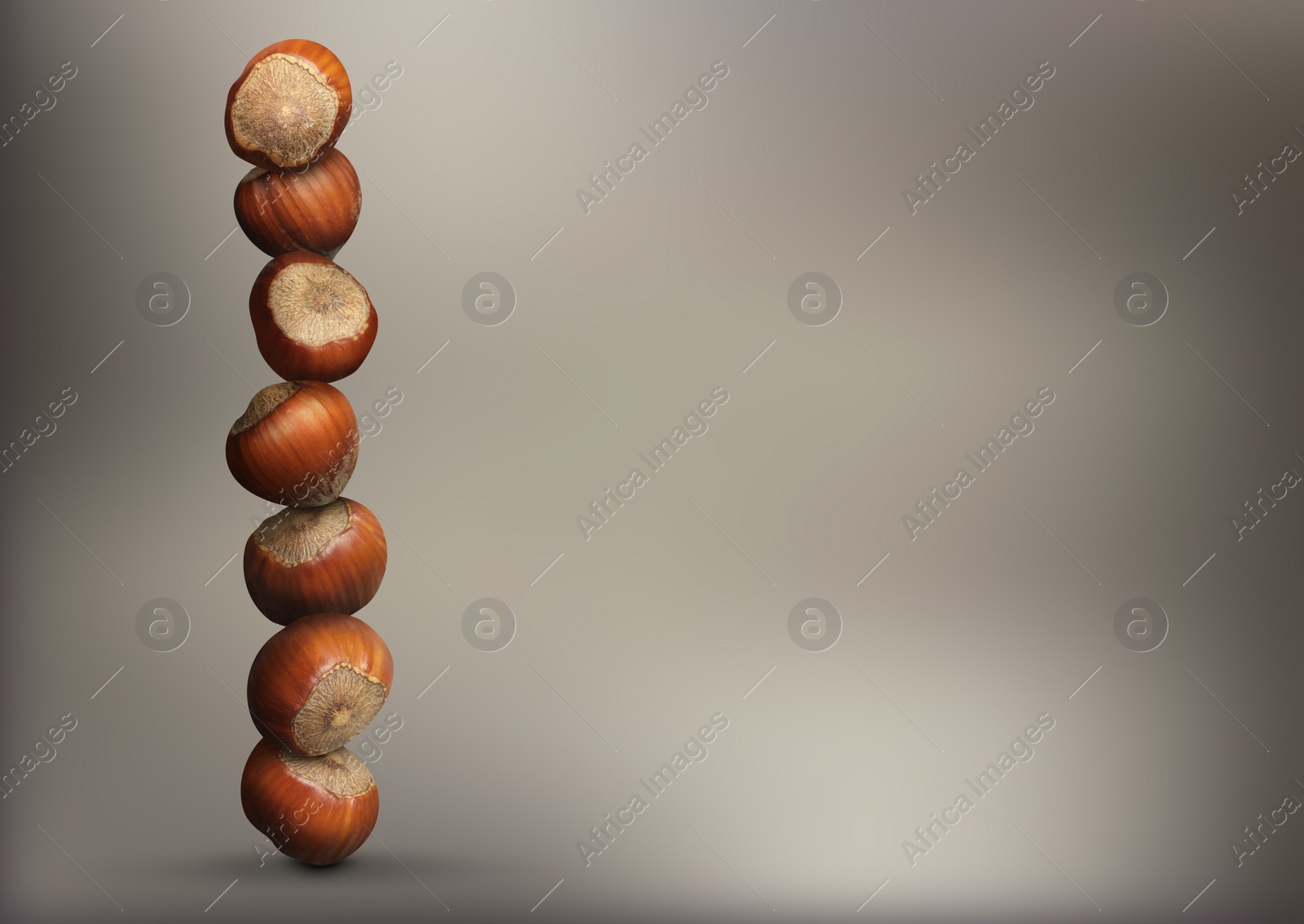 Image of Stacked hazelnuts on light brownish grey gradient background, space for text