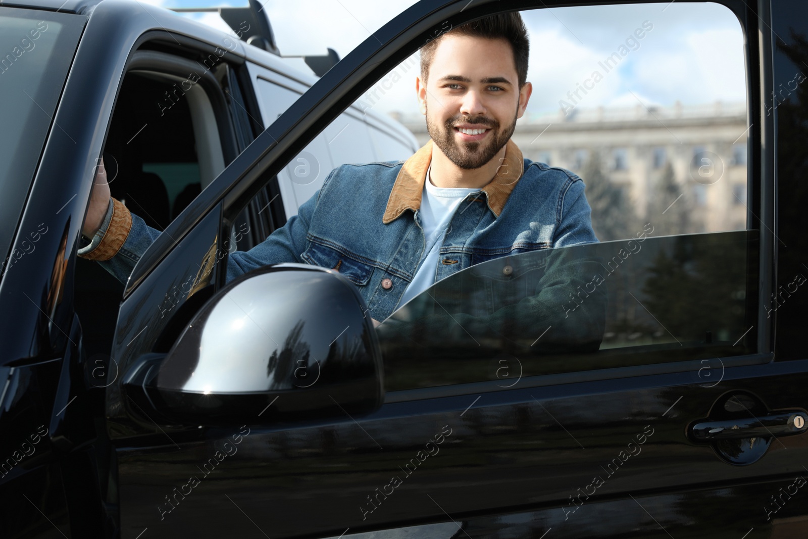 Photo of Handsome young man opening door of modern car outdoors