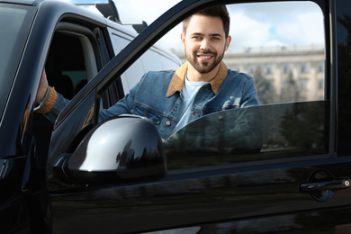 Photo of Handsome young man opening door of modern car outdoors