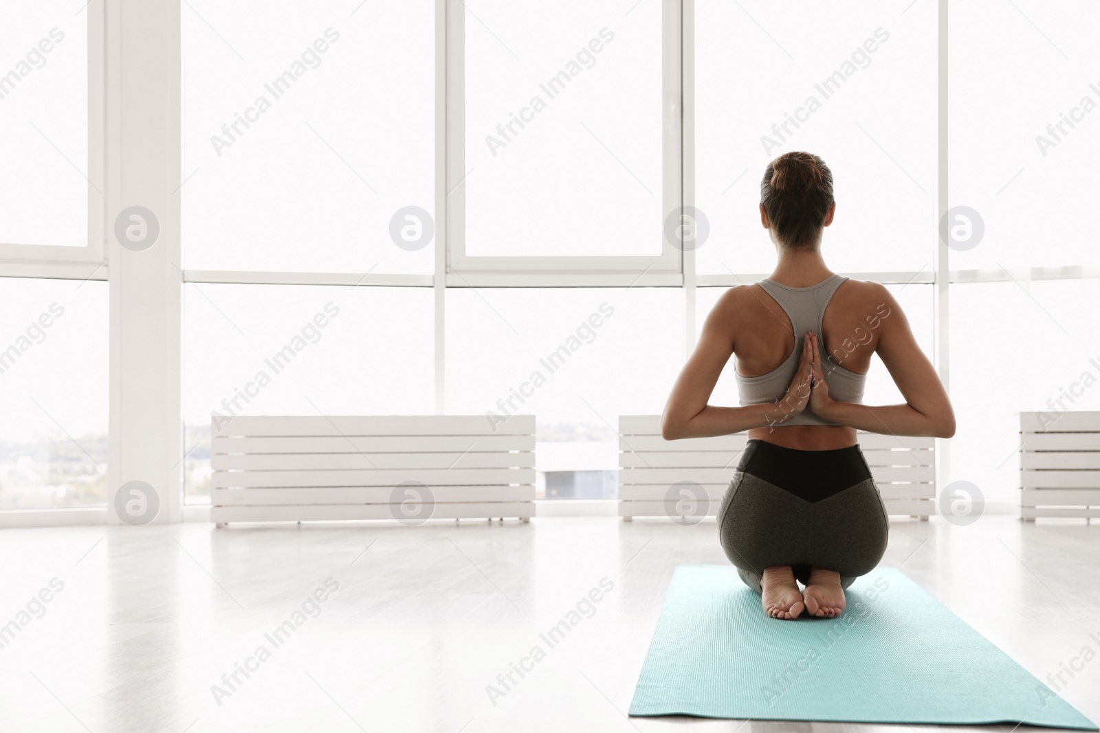 Photo of Young woman practicing thunderbolt asana with reverse prayer arms in yoga studio, back view. Vajrasana Paschima Namaskarasana pose