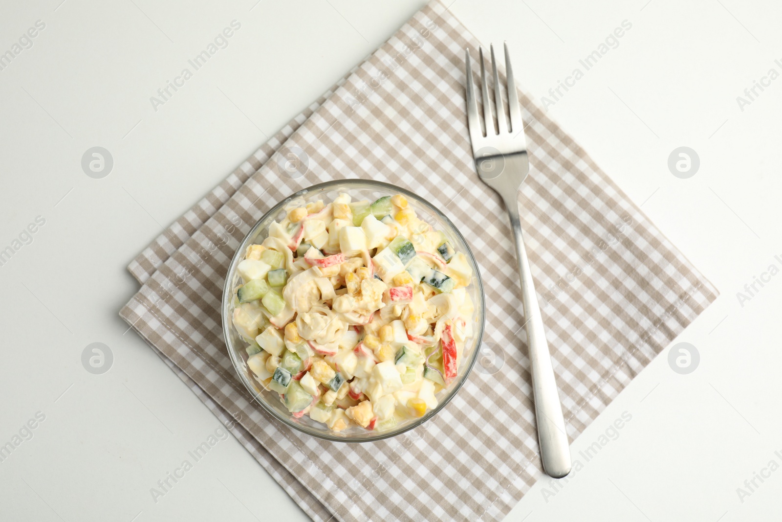 Photo of Delicious salad with fresh crab sticks in glass bowl on white table, top view