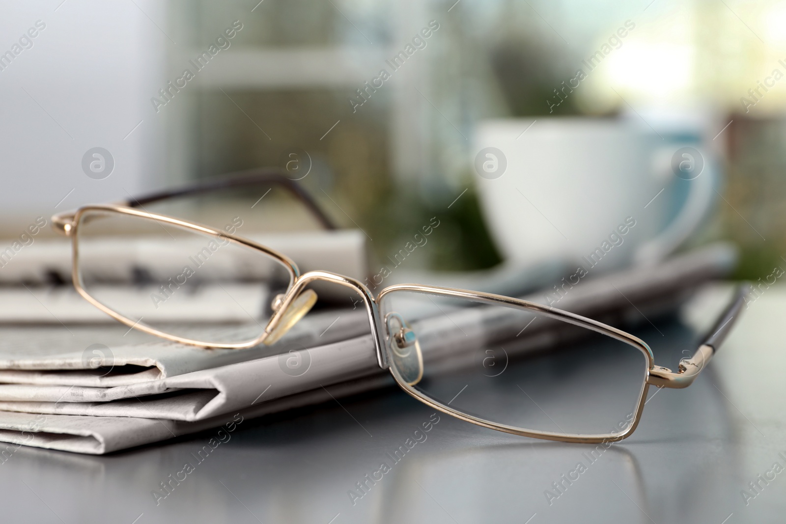 Photo of Stack of newspapers and glasses on grey table indoors, closeup