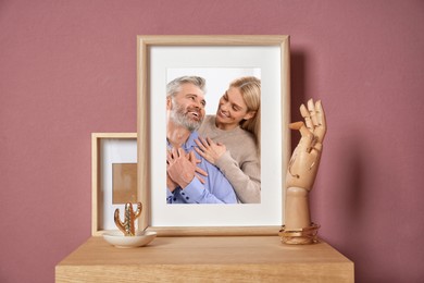 Image of Family portrait of man and woman in photo frame on table near color wall