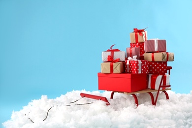 Photo of Sleigh with presents in artificial snow on light blue background. Space for text