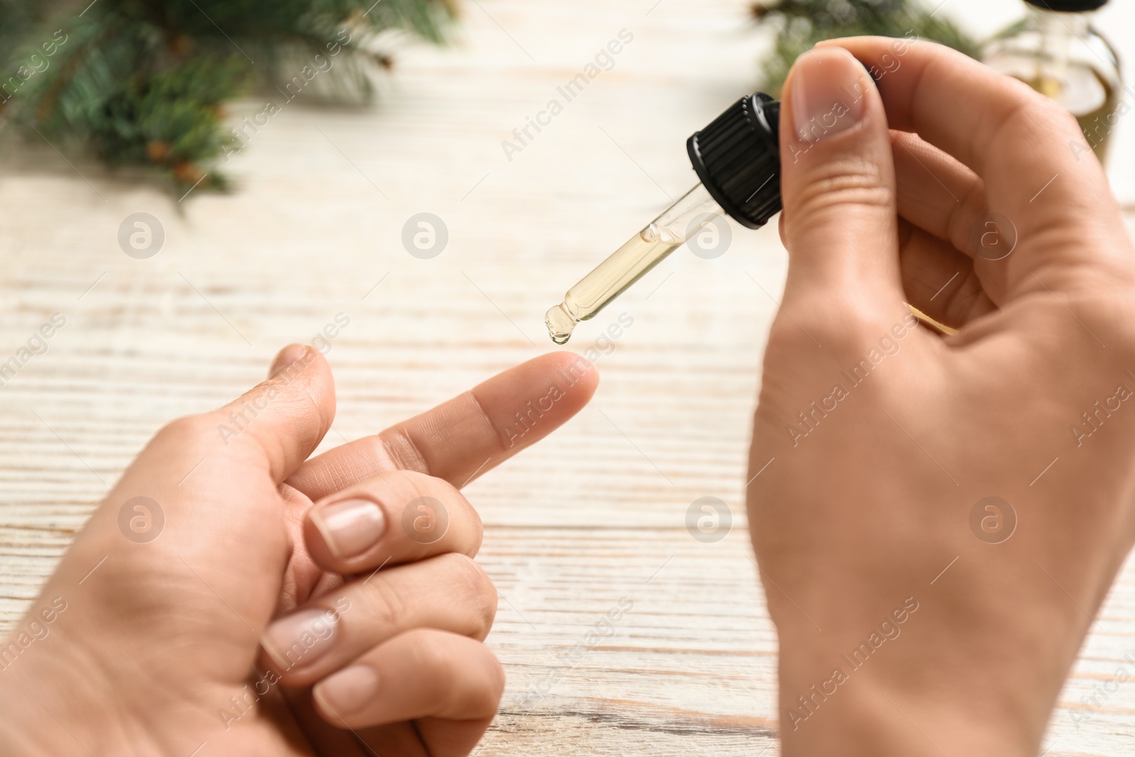 Photo of Woman applying conifer essential oil on finger over white wooden table, closeup