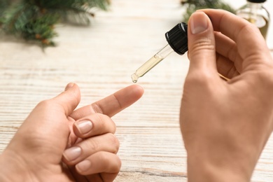 Photo of Woman applying conifer essential oil on finger over white wooden table, closeup