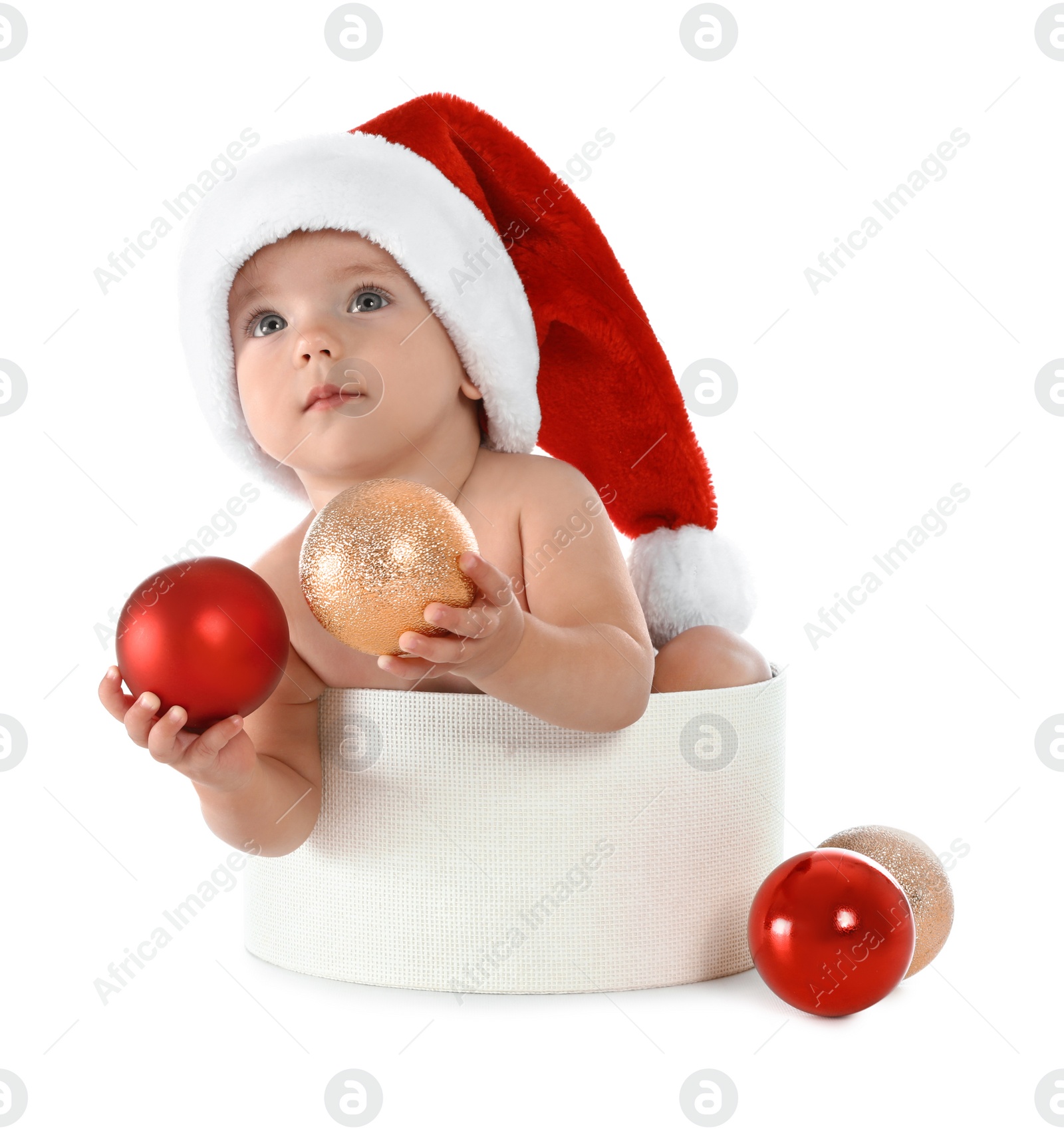 Photo of Cute little baby wearing Santa hat sitting in box with Christmas decorations on white background