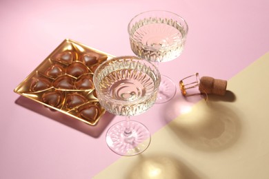 Photo of Glasses of expensive white wine, cork and heart shaped chocolate candies on color background