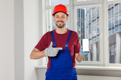 Professional repairman in uniform with phone indoors