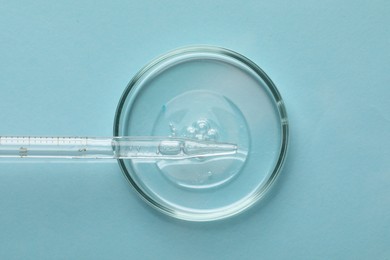 Glass pipette and petri dish with liquid on light blue background, top view