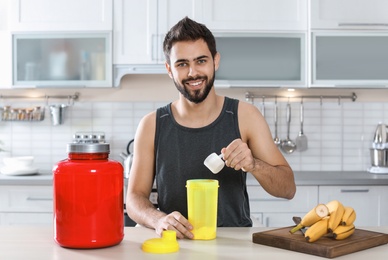 Young man preparing protein shake at table in kitchen