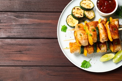 Photo of Delicious chicken shish kebabs with vegetables and sauce on wooden table, top view. Space for text