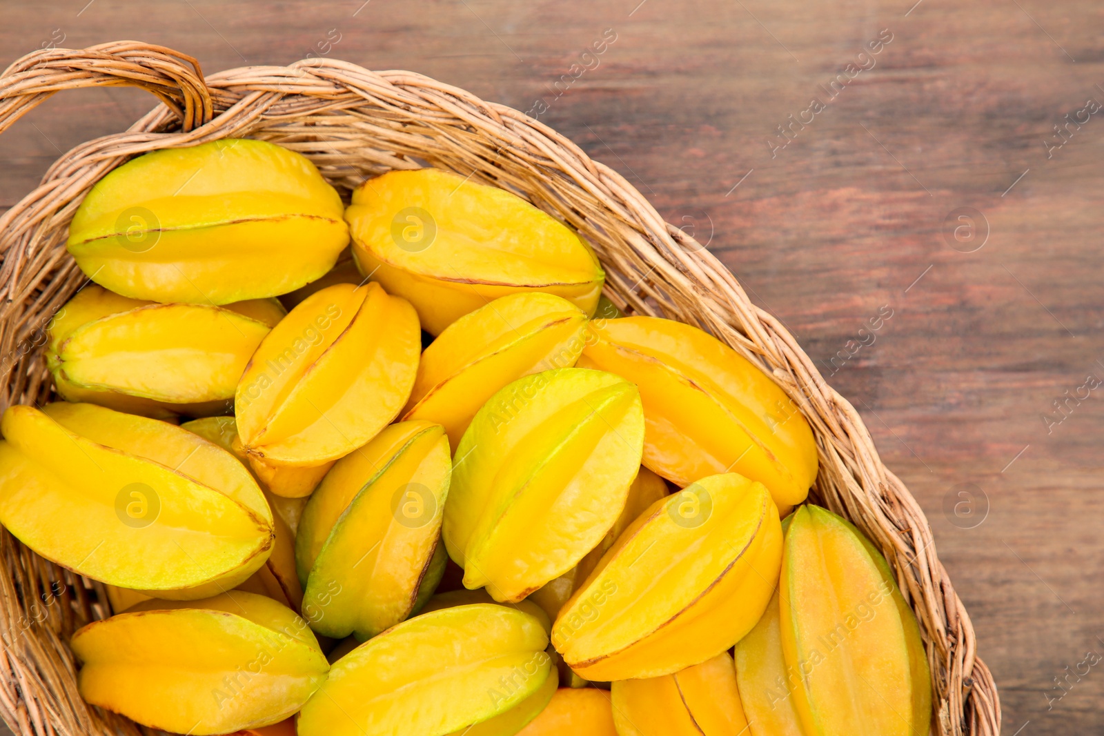 Photo of Delicious ripe carambolas in wicker basket on wooden table