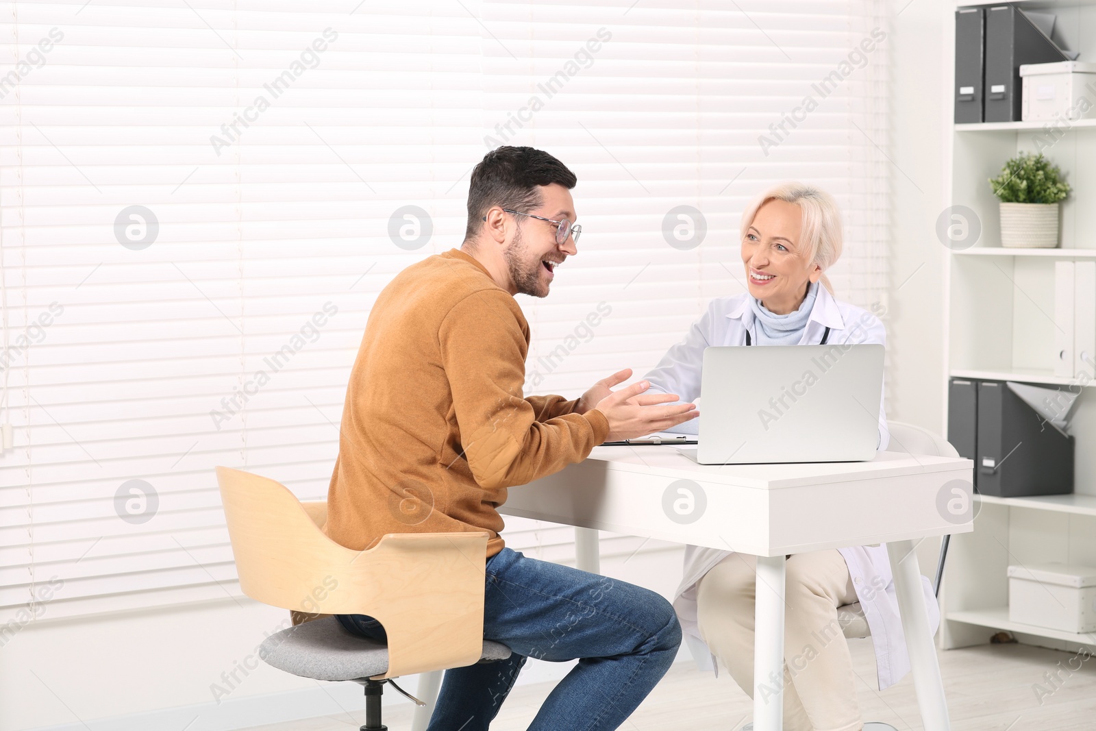 Photo of Doctor and happy patient at white table during consultation in clinic