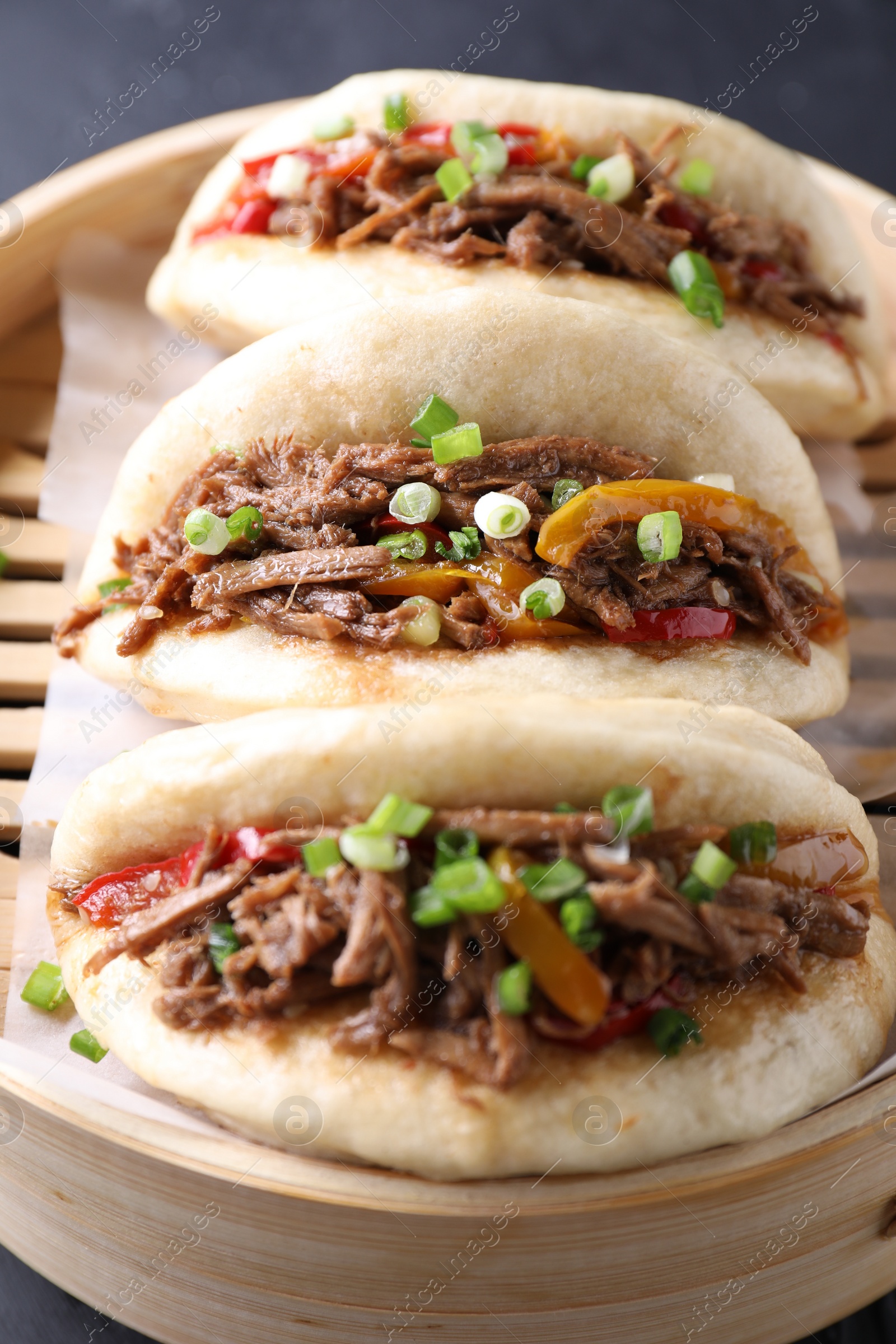 Photo of Delicious gua bao in bamboo steamer on black table, closeup