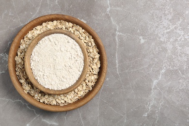 Bowls with oat flour and flakes on grey background, top view. Space for text