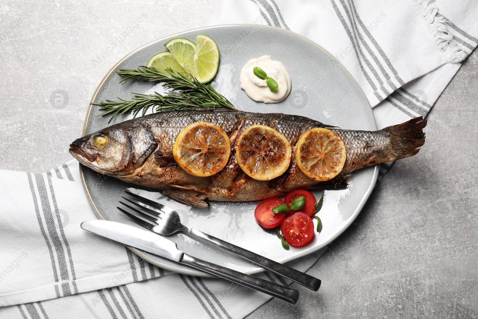 Photo of Delicious roasted sea bass fish served with lemon, rosemary and sauce on light grey table, flat lay