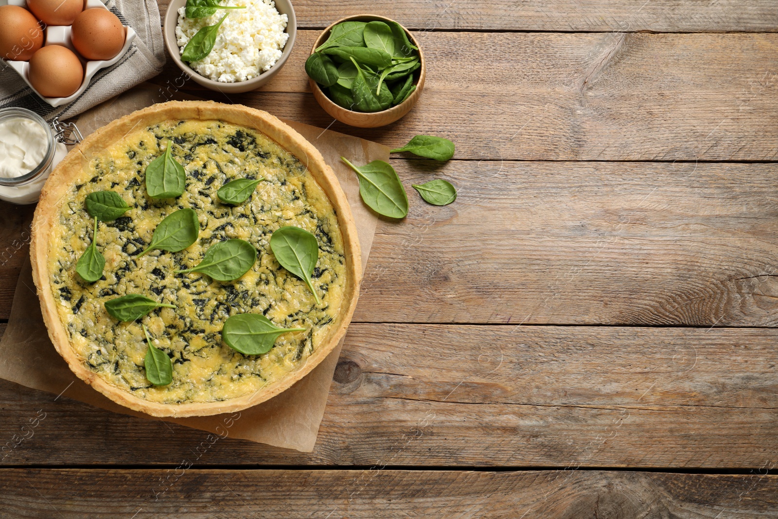 Photo of Delicious homemade spinach pie and fresh ingredients on wooden table, flat lay. Space for text