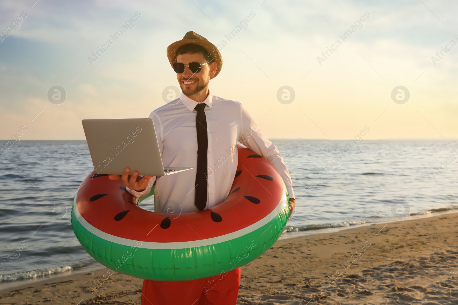 Photo of Happy man with inflatable ring and laptop on beach, space for text. Business trip