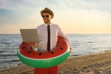 Photo of Happy man with inflatable ring and laptop on beach, space for text. Business trip