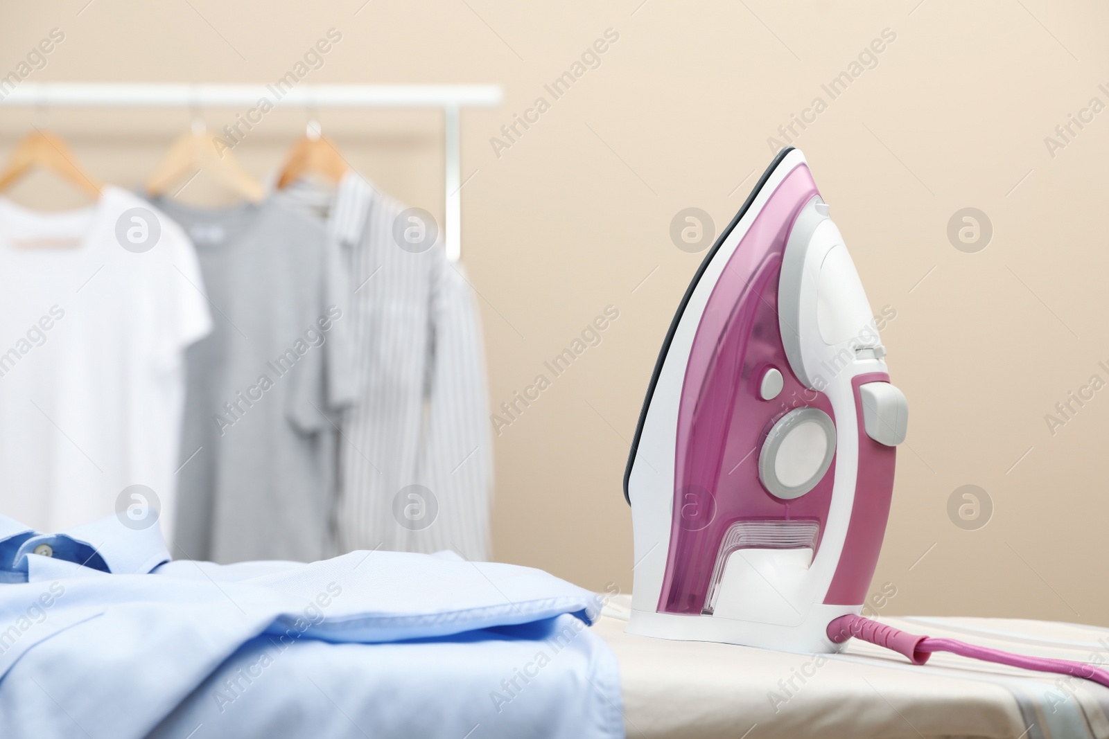 Photo of New modern iron and clean shirt on board against beige background, space for text. Laundry day