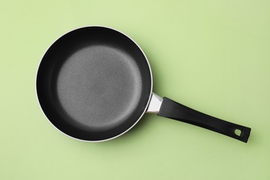One frying pan on light olive background, top view