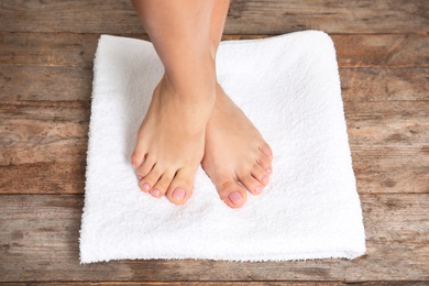 Woman with smooth feet and white towel standing on wooden floor, closeup. Spa treatment