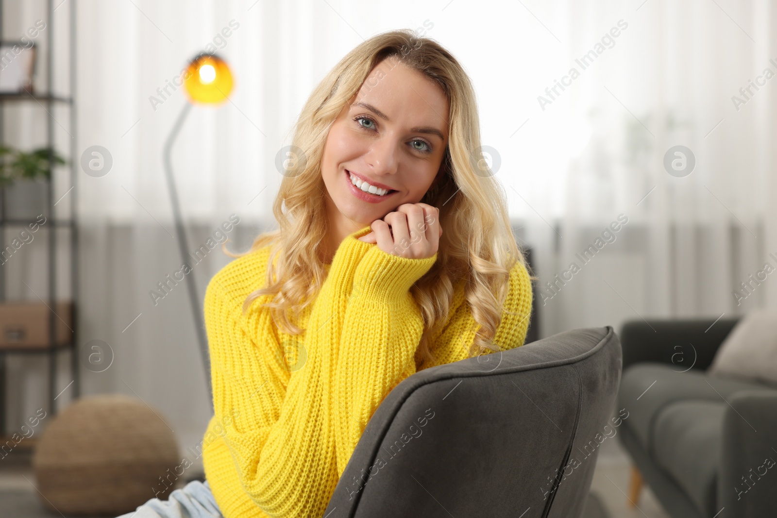 Photo of Happy woman wearing stylish warm sweater in armchair at home