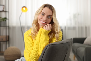 Photo of Happy woman wearing stylish warm sweater in armchair at home