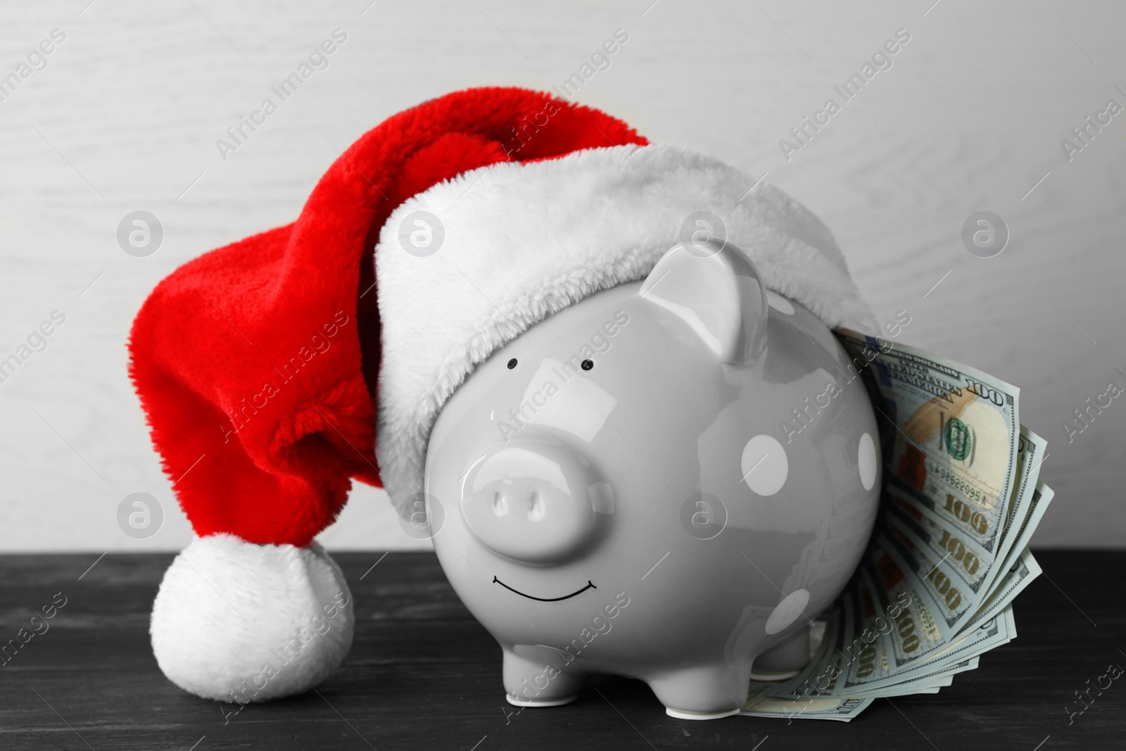 Photo of Piggy bank with Santa hat and dollar banknotes on black wooden table